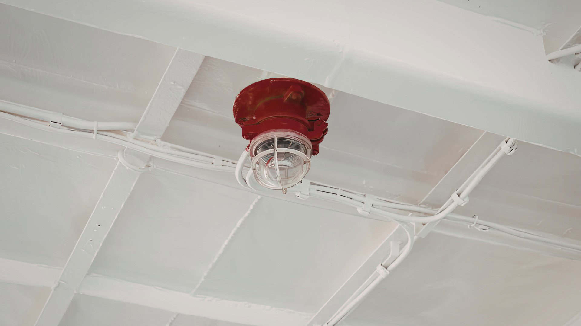 Red and white marine sensor attached to ceiling with wiring.