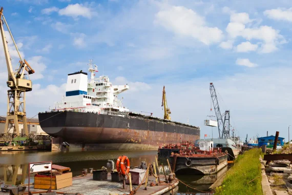 Large vessel in dry dock with cranes and equipment around it.