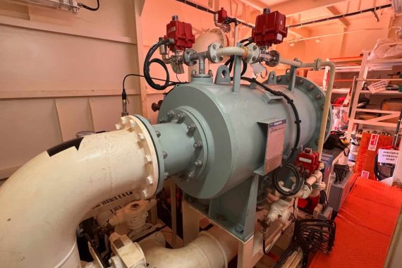 Large industrial marine equipment with pipes and valves in workshop.